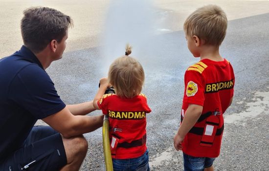 en brandman som hjälper två små barn att använda brandslangen